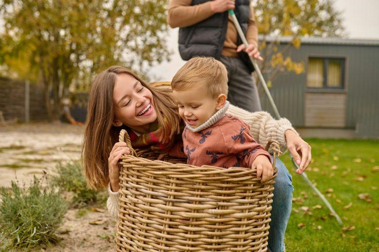 Woman playing with child sitting in basket in garden